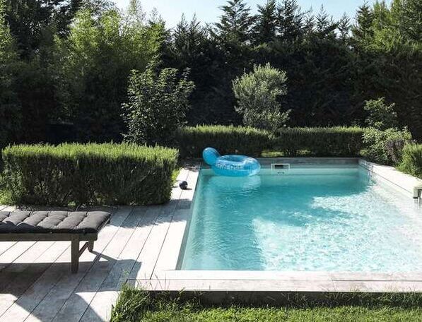 blue swimming pool with greenery surrounding in and a wooden patio